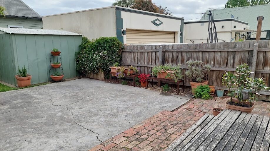 After: Back corner cleared. Self-seeded growth taken out and the paving swept back to clean concrete.